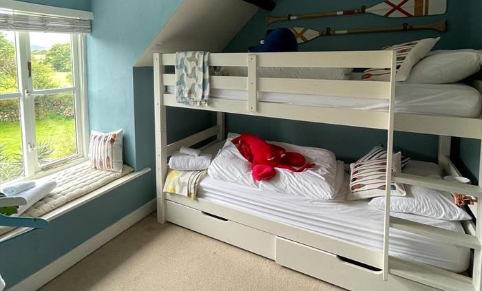 a bunk room with white beds and a soft toy lobster and blue whale with mustard and gray oar cushions and painted oars on the wall